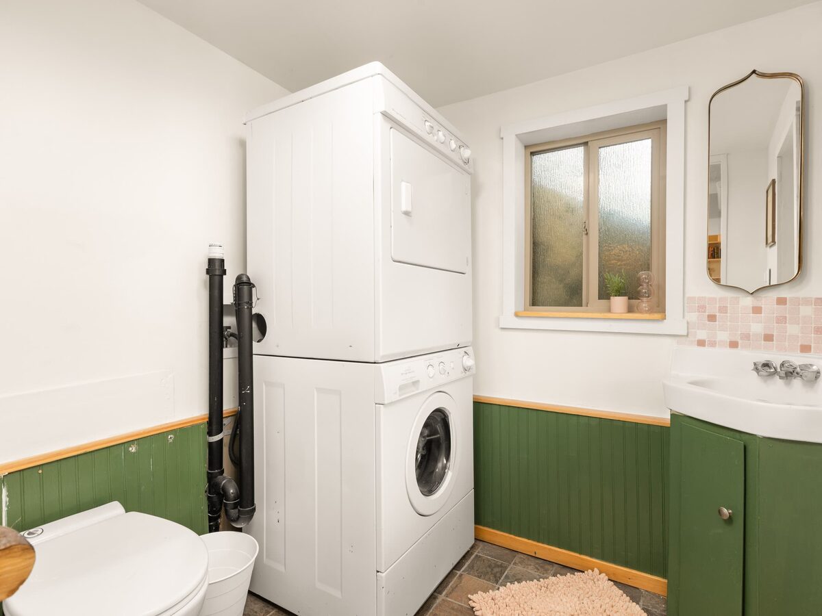 Full bathroom with green vanity, brass mirrors and a stacked washer and dryer